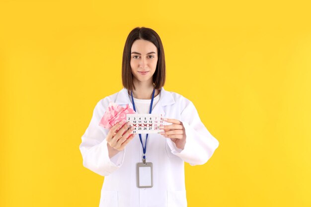 Medico in formazione con pastiglie e calendario mestruale su sfondo giallo