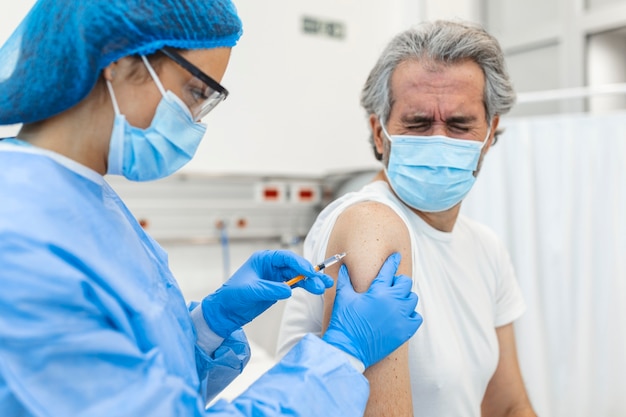 Medico in guanti che tengono la siringa e che fa l'iniezione al paziente anziano nella mascherina medica.