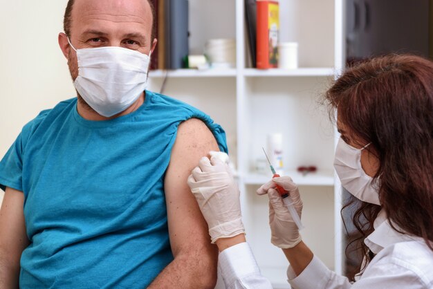 Medico in guanti che tengono la siringa e che fa l'iniezione al paziente nella mascherina medica. Vaccino Covid-19 o coronavirus