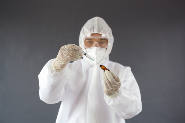 Medico in tuta dpi uniforme che indossa il virus di protezione della maschera facciale che tiene la fiala di vaccino liquido della medicina