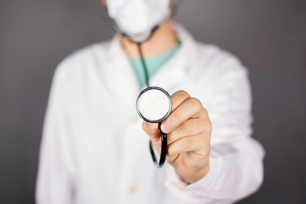 Medico in un abito medico bianco con una maschera usa e getta e uno statoscopio nelle sue mani in piedi