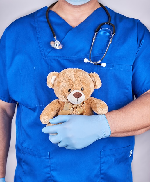 Medico in uniforme blu e vecchi guanti in lattice che tiene un orsacchiotto marrone