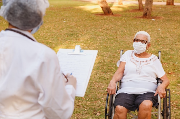 Medico infermiere prendere appunti su appunti consulenza donna anziana nel giardino di casa