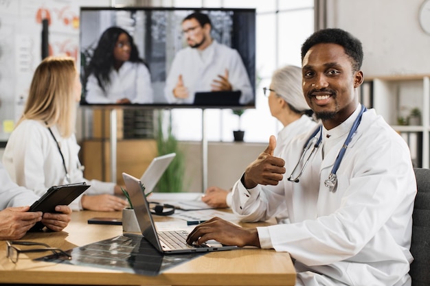 Medico maschio afroamericano con stetoscopio che lavora al computer portatile durante la conferenza online