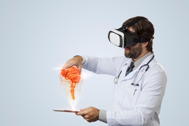 Medico maschio che esamina un cervello virtuale che esce da un tablet su un muro grigio