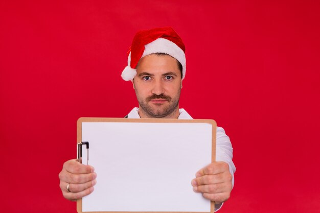 Medico maschio con la barba lunga in cappello di Babbo Natale che tiene appunti in bianco