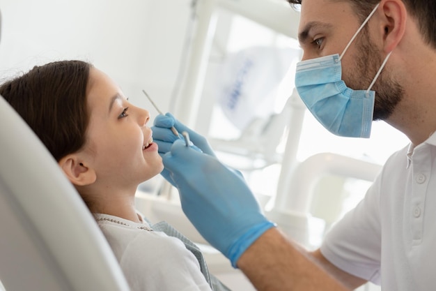 Medico maschio con strumenti nelle mani con ragazza seduta sulla poltrona del dentista