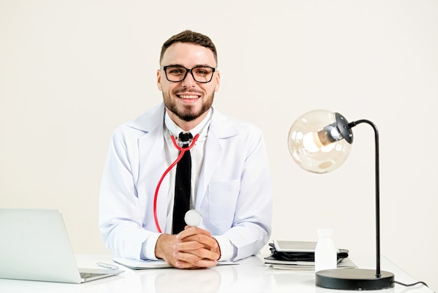 Medico maschio felice alla scrivania in ospedale che lavora al computer portatile. Concetto di assistenza sanitaria medica