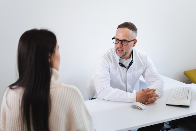 Medico maschio in camice bianco che parla con una paziente nel suo ufficio. Donna che discute del trattamento con il medico durante l'appuntamento in clinica privata