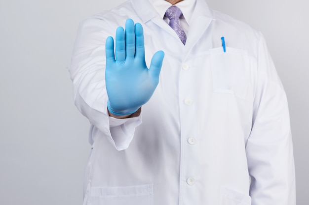 Medico maschio in camice bianco e guanti sterili blu mostra un gesto di arresto