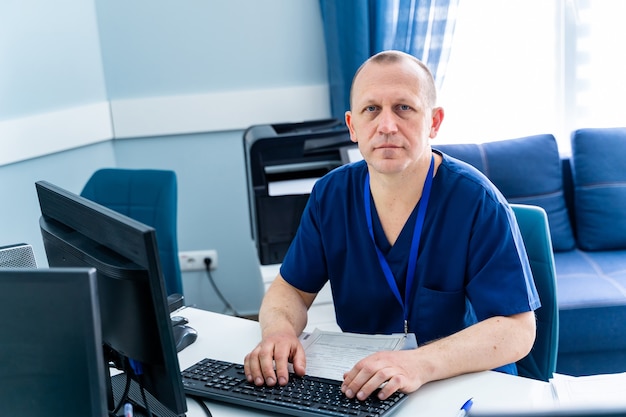 Medico maschio in ufficio che lavora al computer. Fondo moderno dell'ufficio dell'ospedale.