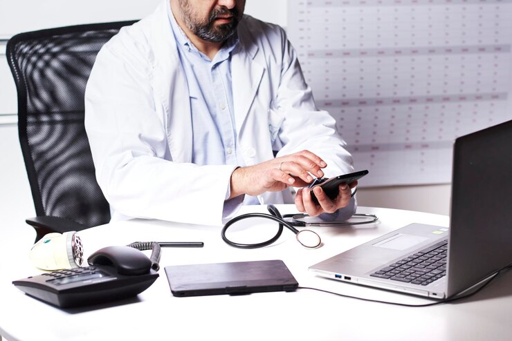 Medico maschio irriconoscibile che utilizza lo smartphone guardando il suo telefono cellulare mentre lavora