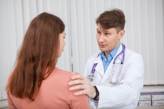Medico maschio maturo che lavora nella sua clinica, parlando con un paziente di sesso femminile. Medico esperto che conforta il suo paziente sconvolto
