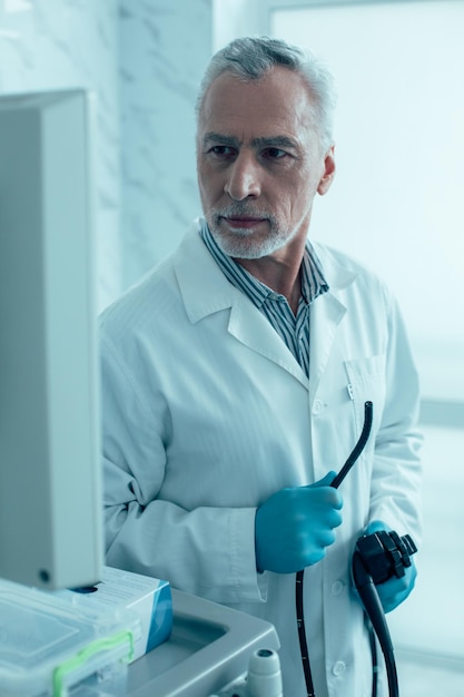 Medico maschio professionista in uniforme medica e guanti di gomma in piedi con un endoscopio e guardando il monitor