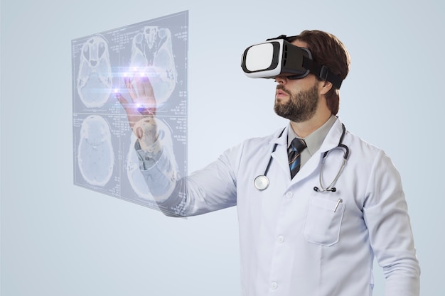 Medico maschio su un muro grigio, utilizzando occhiali per realtà virtuale, guardando uno schermo virtuale