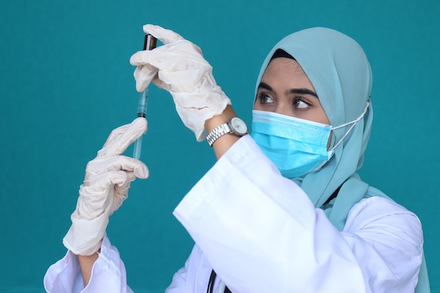 Medico musulmano femminile in hijab che indossa guanti protettivi e maschera medica con siringa per iniezione w