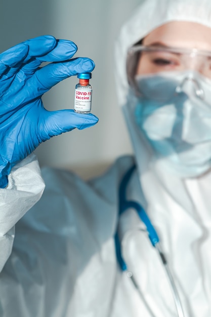 Medico o infermiere in una tuta protettiva che tiene in mano il vaccino covid 19