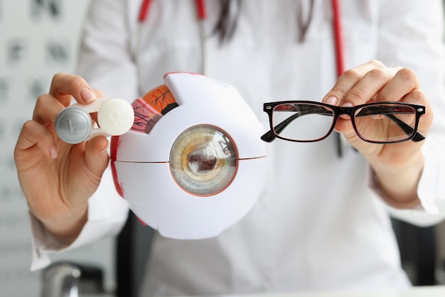 Medico oculista che tiene occhiali e lenti vicino al modello artificiale del primo piano dell'occhio
