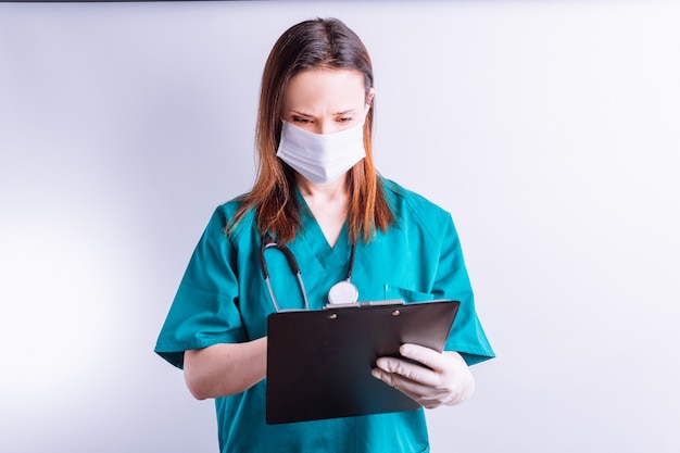 Medico ospedaliero con guanti maschera su sfondo bianco che legge una medicina completa del rapporto