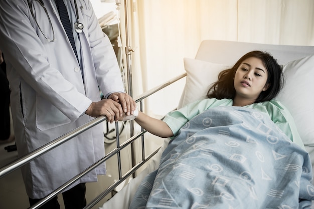 Medico parlando con paziente e tenendo la mano per confortarla. Paziente femminile che ha ferita che si trova sul letto all&#39;ospedale.