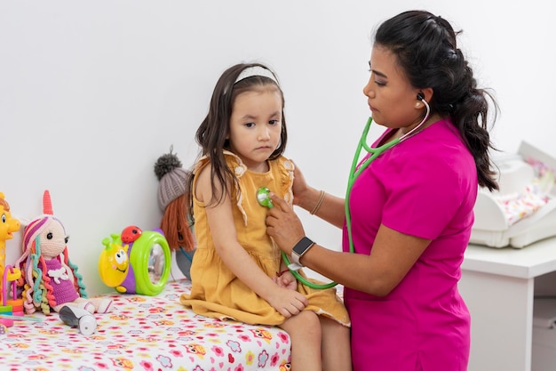 Medico pediatra che controlla con lo stetoscopio una bambina seduta su una barella