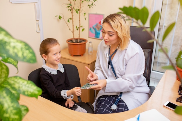 Medico pediatra che esamina un bambino in uno studio medico confortevole. Concetto di assistenza sanitaria, infanzia, medicina, protezione e prevenzione. La bambina si affida al dottore. Divertirsi mentre si prendono le pillole