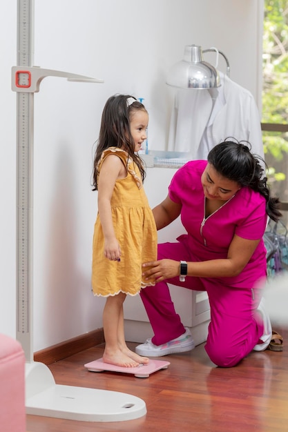 Medico pediatra che pesa una ragazza su una bilancia da pavimento nel suo ufficio