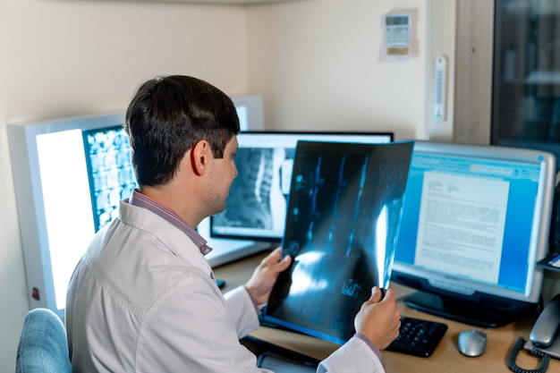 Medico radiologo seduto vicino al computer. Diagnosi al monitor. Vista dal retro. Concetto di neurochirurgia.