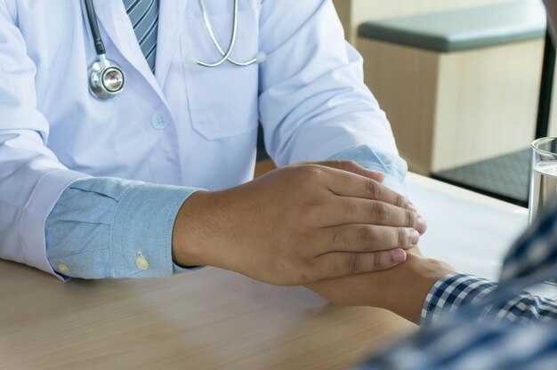 Medico sanitario Medico professionista in abito bianco uniforme cappotto intervista consultazione paziente rassicurando il suo paziente di sesso maschile aiutando la mano