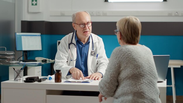 Medico senior che fa consulenza di controllo con un paziente malato in pensione in studio medico, parlando della diagnosi della malattia. Conversazione sulla malattia, il recupero e il trattamento di prescrizione.