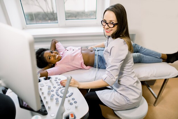 Medico sorridente della donna e il suo paziente femminile africano nella stanza diagnostica di ultrasuono