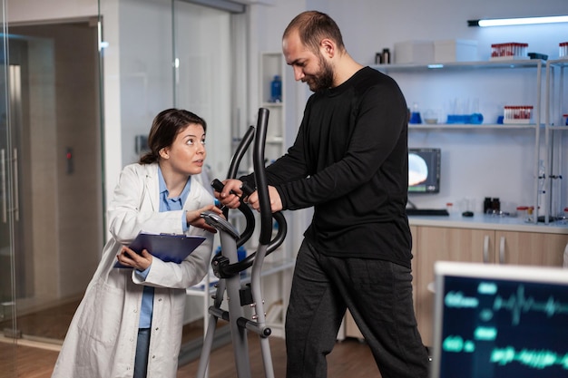 Medico specialista che parla con lo sportivo in attrezzature per l'allenamento in palestra che monitorano la resistenza del corpo durante l'allenamento medico in un moderno laboratorio. Medico ricercatore che analizza i dati dell'elettrocardiogramma