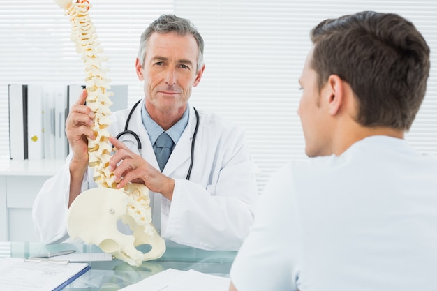 Medico spiegando la colonna vertebrale al paziente in ufficio
