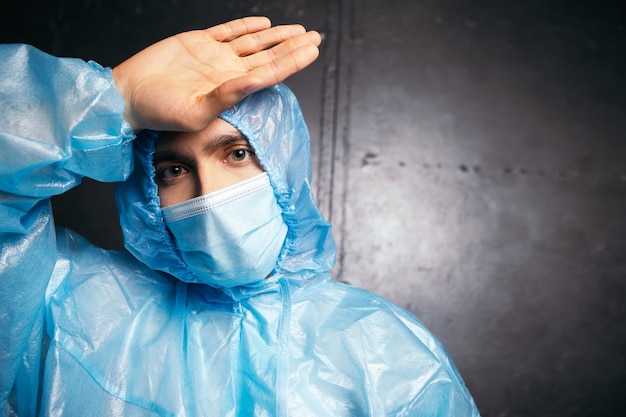 Medico stanco in piedi vicino al muro che indossa tuta protettiva e maschera facciale