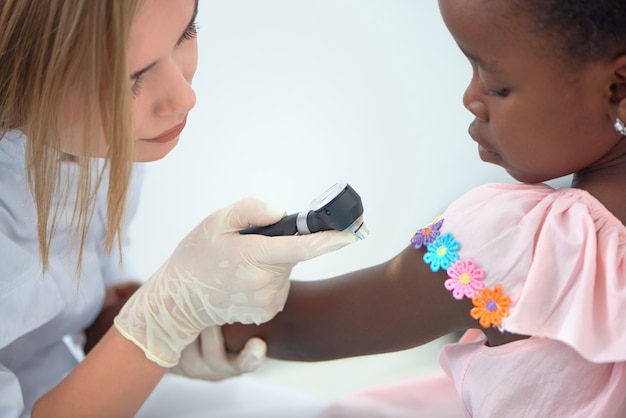 Medico sveglio che controlla pelle sulle spalle di piccola ragazza afro.