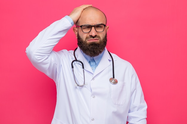 Medico uomo barbuto in camice bianco con stetoscopio intorno al collo con gli occhiali che sembra confuso e molto ansioso tenendo la mano sulla testa per errore