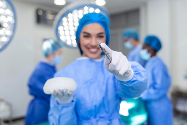 Medico urgente sorridente che tiene protesi mammaria al silicone nelle mani del chirurgo