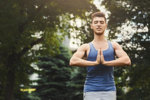 Meditando l'uomo con le mani in preghiera all'aperto. Uomo sereno che pratica yoga e si rilassa nel parco, copia spazio