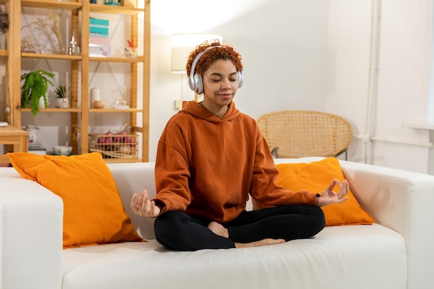 Meditazione di consapevolezza yoga Giovane ragazza africana in buona salute che pratica yoga a casa Donna seduta nella posa del loto sul tappetino yoga meditando sorridente rilassante al coperto Ragazza che fa pratica di respirazione yoga a casa