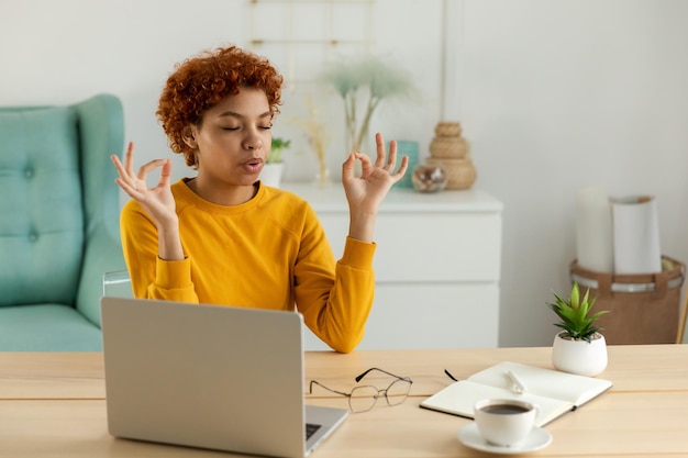 Meditazione di consapevolezza yoga Nessuno stress mantieni la calma Ragazza africana che pratica yoga in ufficio a casa Donna nella posa del loto al tavolo dell'ufficio meditando rilassante al coperto Ragazza che fa pratica di respirazione al lavoro