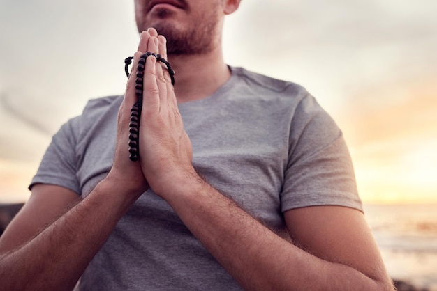 Meditazione spirituale e mani di un uomo in spiaggia che prega per la pace e il benessere in Indonesia Yoga zen e persona con una preghiera per gratitudine adorazione e guarigione nella natura sull'oceano