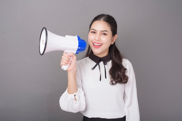 Megafono asiatico bello della tenuta della donna sullo studio grigio del fondo