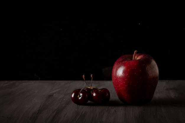 Mela accompagnata da ciliegie su un tavolo nero vintage con spazio per il testo