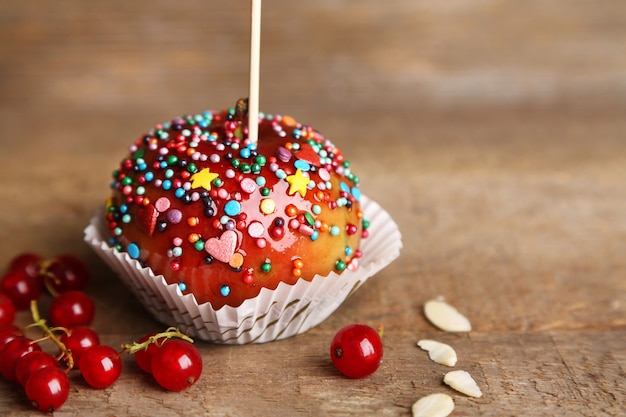 Mela caramellata dolce su stecco con frutti di bosco, su tavola di legno