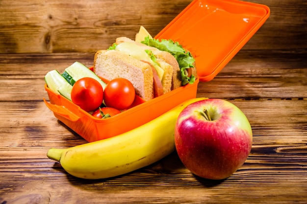 Mela matura banana e pranzo al sacco con panini cetrioli e pomodori sul tavolo di legno