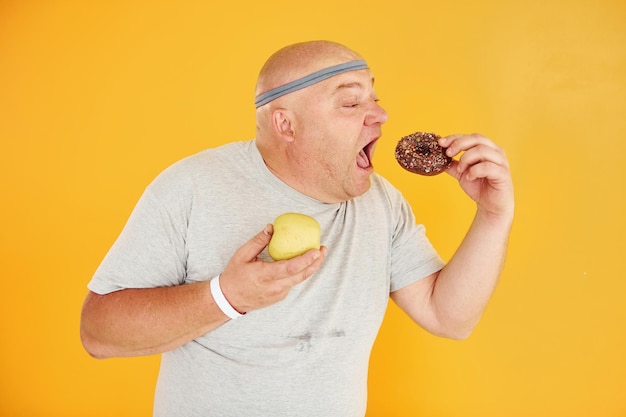 Mela o biscotto Divertente uomo sovrappeso in cravatta sportiva è su sfondo giallo
