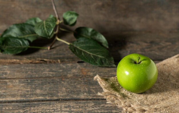 Mela verde con foglie su tela da imballaggio su tavole di legno