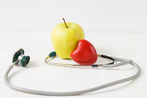 Mela verde, cuore rosso e stetoscopio su uno sfondo chiaro