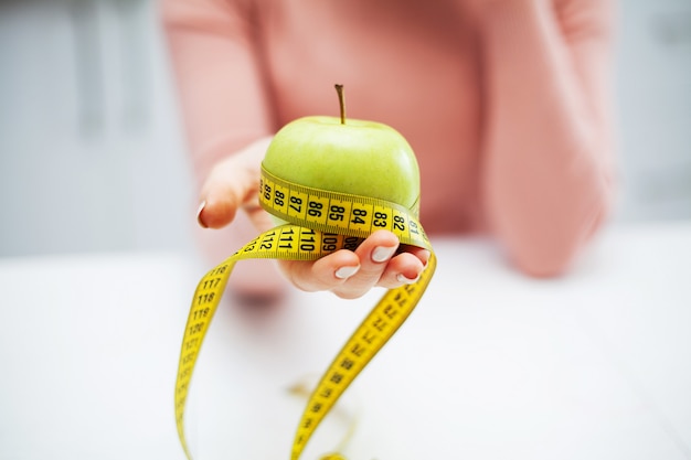 Mela verde e nastro di centimetro in mani femminili