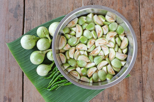 Melanzana organica fresca affettata in acqua e peperoncini rossi verdi sulla foglia della banana contro la tavola di legno